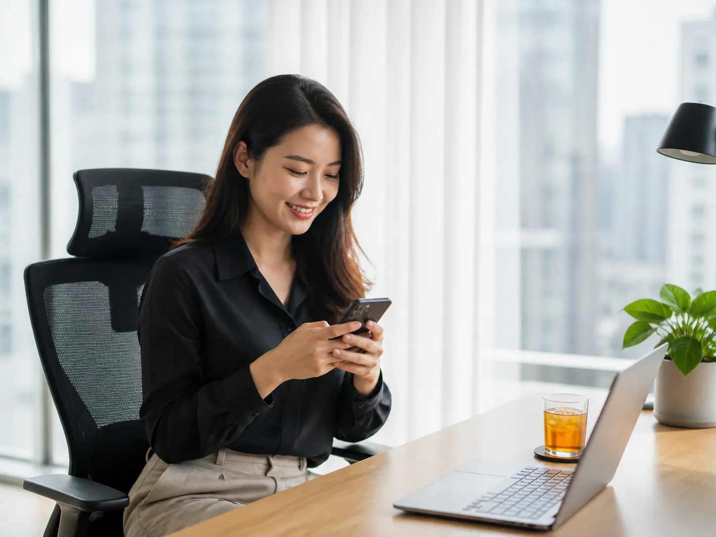 A working professional using her phone beside a laptop in a bright home office